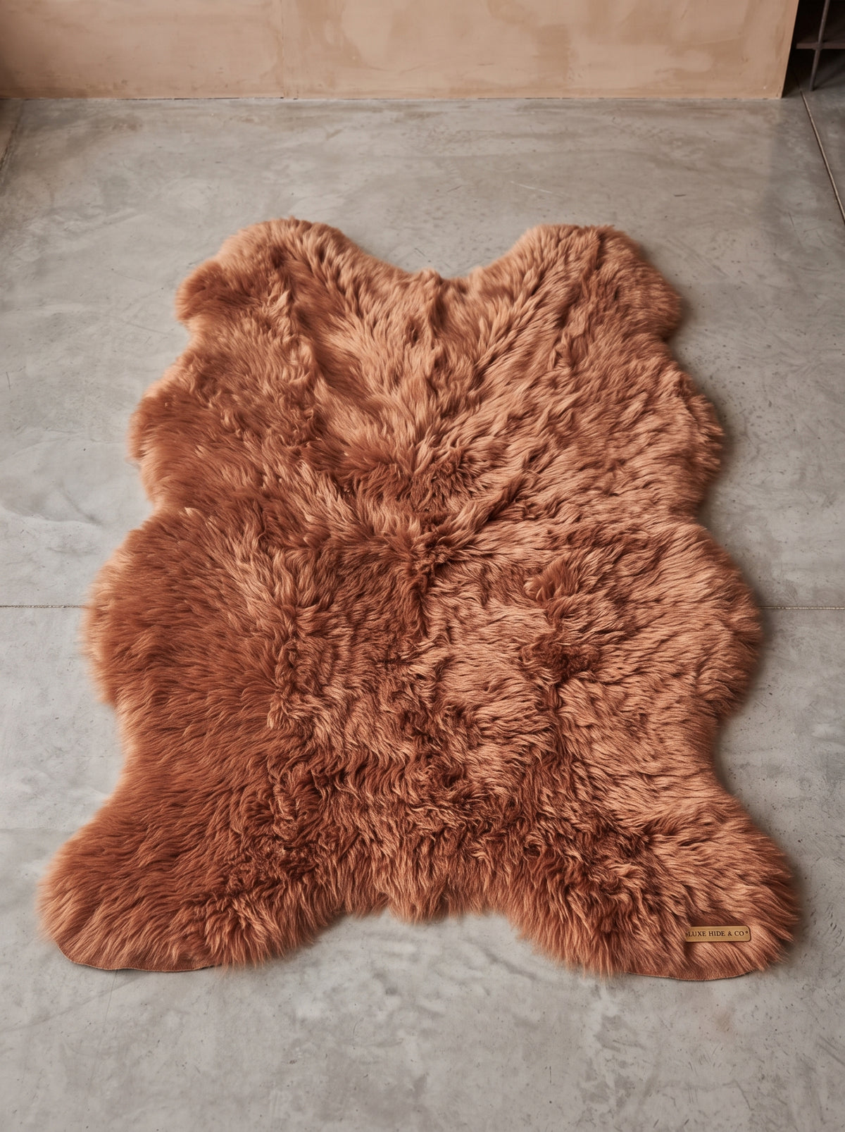 A brown shaggy faux fur rug laid flat on a gray tiled floor against a beige wall.