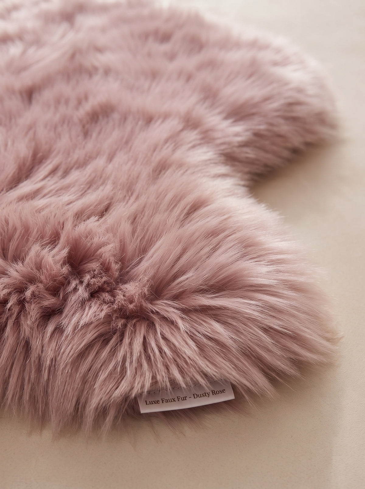 A close-up of a dusty pink faux fur rug with a small fabric tag reading 'Instant Fur Co - Dusty Rose' on a neutral beige background.