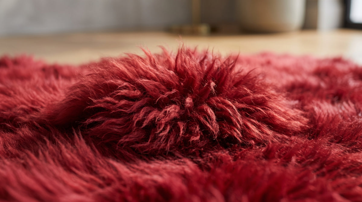 A close-up of a plush, shaggy red rug with a textured, fluffy pile, shown in a softly blurred indoor setting.