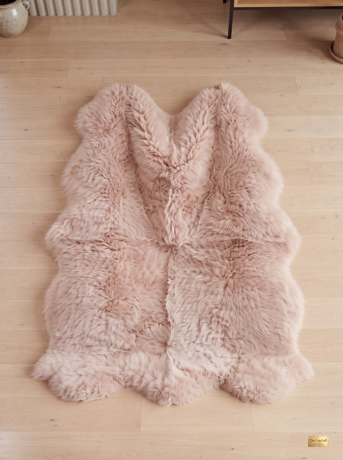 A fluffy pale blush pink sheepskin rug laid flat on a light wood floor.