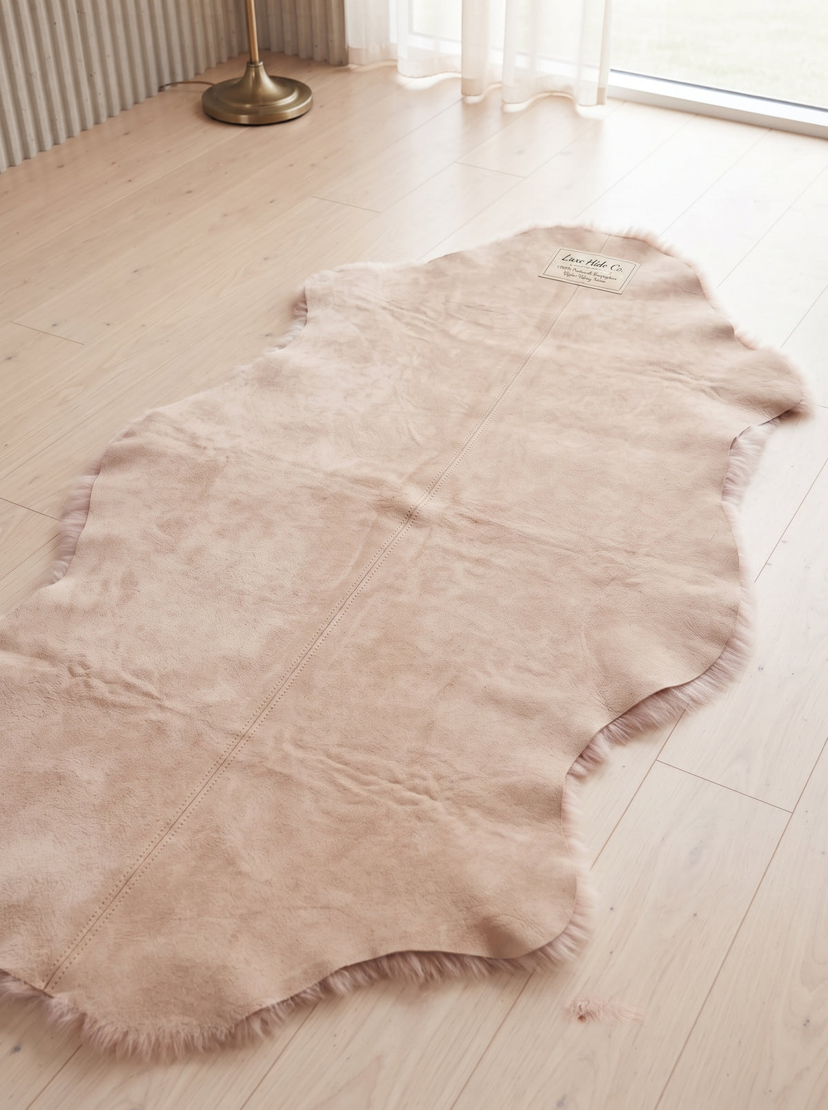 A natural cowhide rug in a light beige/tan color, laid out on a light wood floor in a bright room near a window.