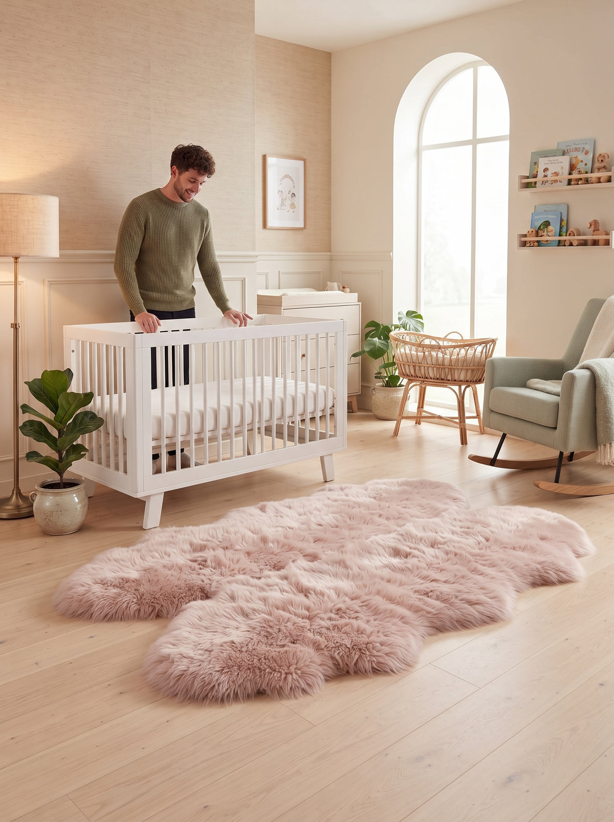 A fluffy pale pink shag rug laid on a light wood floor in a softly styled nursery, with a man standing beside a white crib and a green armchair nearby.